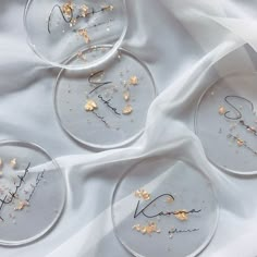 four glass plates with flowers on them sitting on a white cloth covered tablecloth in the shape of letters