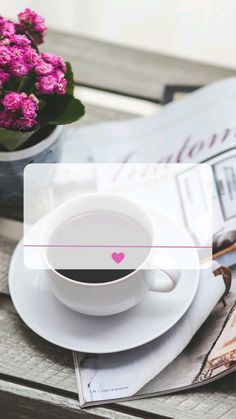 a cup of coffee sitting on top of a white plate next to a vase with pink flowers