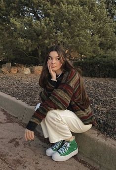 a woman sitting on the side of a road with her hand under her chin and looking at the camera