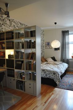 a bedroom with a bed, bookshelf and desk in the corner next to a window