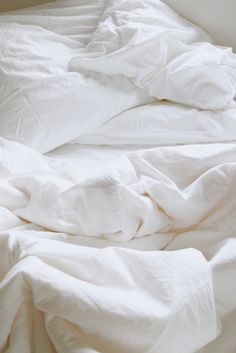 an unmade bed with white sheets and pillows