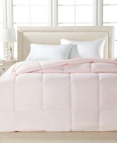 a pink comforter on a white bed in a room with windows and nightstands