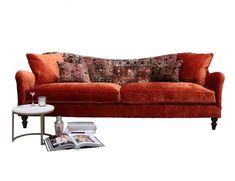 an orange couch with pillows on it next to a coffee table and magazine holder in front of it