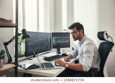 a man sitting at a desk in front of two computer monitors with graphs on them