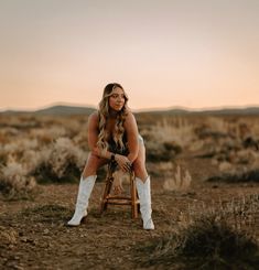 a woman sitting on top of a wooden chair in the middle of a desert field