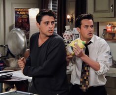 two men standing in a kitchen one holding a banana and the other looking at something