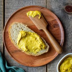 a wooden plate topped with bread covered in yellow sauce next to a bowl of mustard