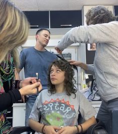 a woman is getting her hair cut by two men in an office setting with other people