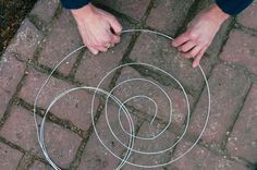 two hands holding an object in the middle of a circle on a brick sidewalk with grass and dirt around it