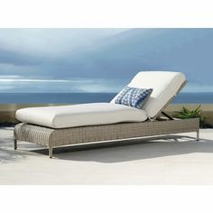 an outdoor chaise lounge with blue and white pillows on the top, overlooking the ocean