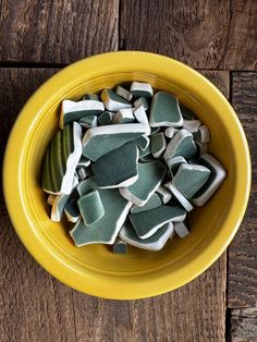 a yellow bowl filled with sea glass on top of a wooden table