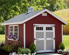 a red and white shed with flowers in the window box next to it on a green lawn