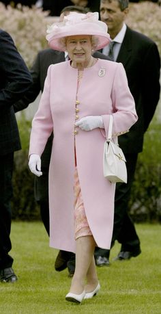 an older woman in a pink coat and hat walks through the grass with other people