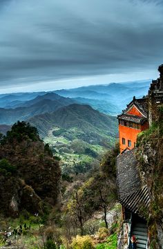 an orange building on the side of a hill with mountains in the background and people walking up it