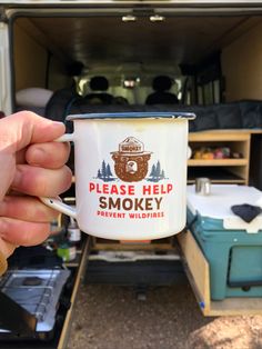 someone holding up a coffee cup with the words please help smokey in front of their camper