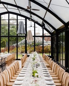 a long table set up for an event in a glass walled room with large windows