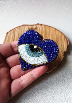 a hand holding a blue and white heart shaped brooch with an eye on it