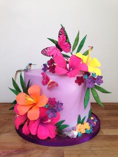 a purple cake with flowers and butterflies on the top is sitting on a wooden table