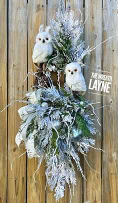 two stuffed owls sitting on top of a fake wreath covered in frosty branches and pine cones