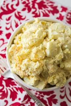 a white bowl filled with potato salad on top of a red and white place mat