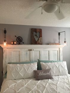 a white bed topped with pillows next to a wall mounted fan and light fixture above it