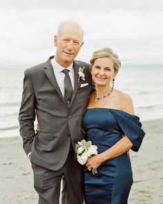 an older man and woman standing next to each other on the beach in front of the ocean