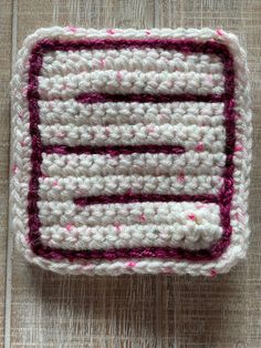 a crocheted dishcloth with pink and white stripes on it sitting on a wooden surface