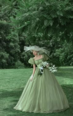 a woman in a green dress and veil is standing under a tree with her hands on her hips