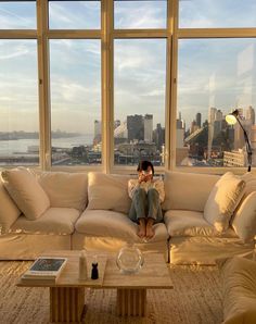 a woman sitting on top of a couch in front of a window next to a coffee table