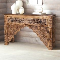 an ornate wooden table with two vases on it and a mirror in the corner