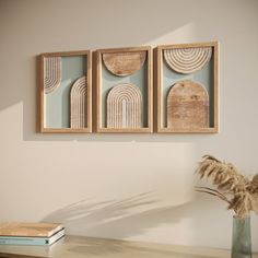 three framed art pieces hang on the wall above a vase with dried grass in it