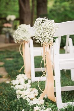 two white chairs with flowers tied to them on the grass and one chair is decorated with baby's breath