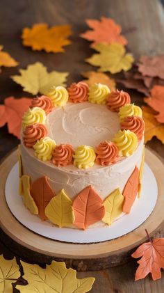 a white cake with orange and yellow frosting on a wooden table surrounded by fall leaves