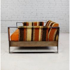 an orange and brown striped couch sitting on top of a white floor next to a brick wall