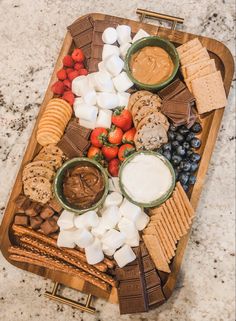 a wooden platter filled with cheese, crackers and fruit