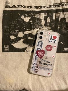 an iphone case with stickers on it sitting next to a t - shirt that says i love new york