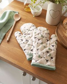 two oven mitts sitting on top of a wooden counter next to a potted plant