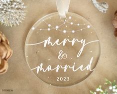 a glass ornament with the words merry and married on it next to pine cones