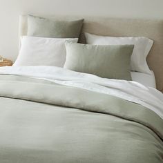 an unmade bed with white linens and pillows on the headboard, along with a wicker basket