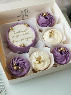 four cupcakes with white frosting and purple icing are in a box