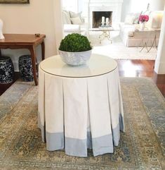 a white table topped with a bowl filled with green plants on top of a rug