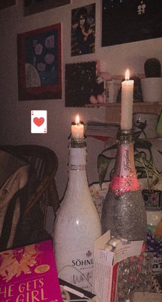 two wine bottles with candles in them sitting on a table next to books and other items