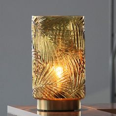 a golden vase sitting on top of a table next to a light bulb in the shape of a palm leaf