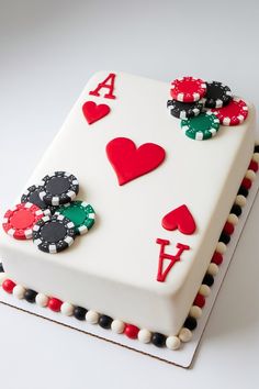 a white cake decorated with playing cards and hearts on it's sides, sitting on top of a table