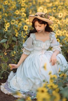 a woman in a dress and hat sitting in a field of sunflowers