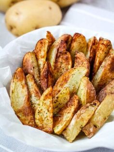 cooked potatoes in a white bowl on top of a table next to potato wedges