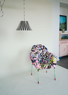 a colorful chair sitting on top of a white floor next to a light hanging from the ceiling