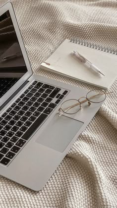 an open laptop computer sitting on top of a bed next to a pen and glasses