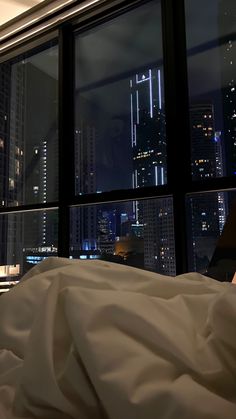 a person laying in bed looking out the window at cityscape and skyscrapers