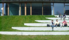 three people sitting on concrete steps in front of a building with grass growing up the side